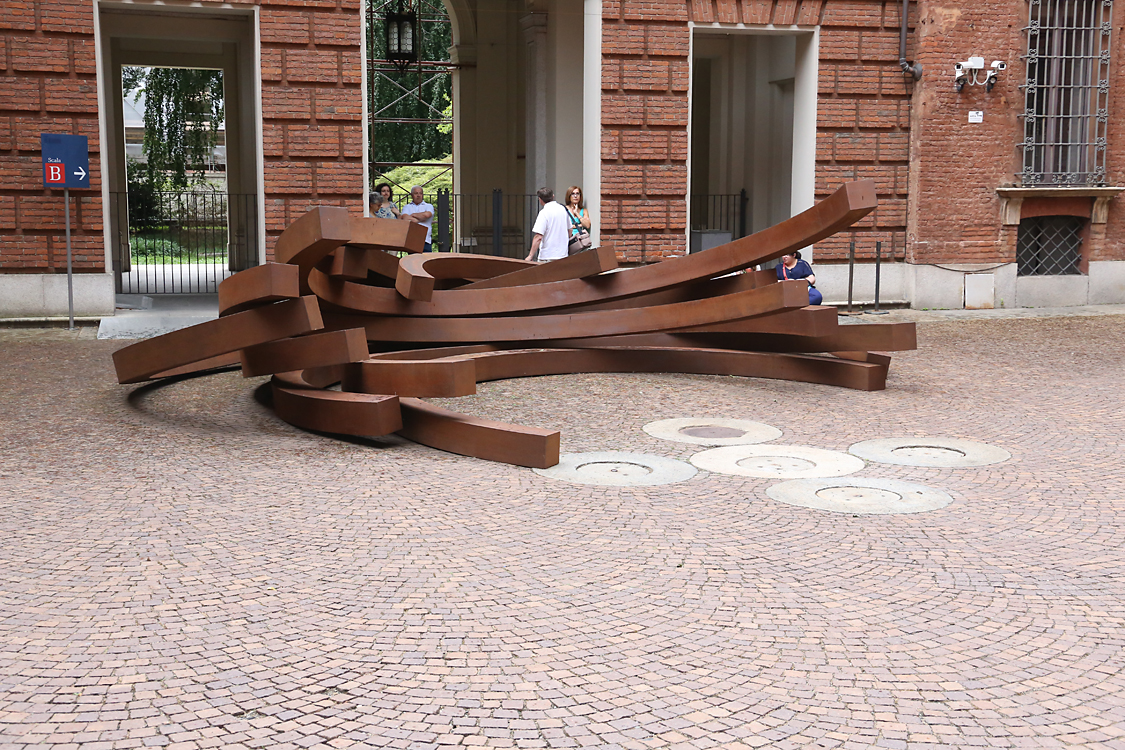 ArteAlleCorti_080.jpg - Bernar VENET - Effondrement: 217.5° Arc x 11 - Palazzo Cisterna La monumentale scultura, composta da undici elementi arcuati a 217.5° in acciaio Cor-Ten, pare collassare suse stessa, in un misterioso campo di forze che pone gli archi in un coerente dialogo tra ordine e disordine, tradinamismo e potenza: una “Action Sculpture in slow motion” come la defi nisce l’artista stesso. Un’applicazionedella teoria del caos all’oggetto artistico dove la materia non è usata per creare forme, è essa stessa forma.