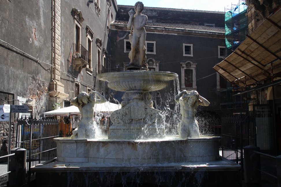 Sicilia_159.JPG - su un lato della piazza del Duomo fontana dell'Amenano, scolpita da Tito Angelini nel 1867, in marmo di Carrara, rappresenta il fiume Amenano come un giovane che tiene una cornucopia dalla quale fuoriesce dell'acqua che si versa in una vasca dal bordo bombato. L'acqua, tracimando da questa vasca, produce un effetto cascata che dà la sensazione di un lenzuolo. Da qui il modo di dire in siciliano "acqua a linzolu" per indicare la fontana. L'acqua che cade dalla vasca si riversa nel fiume sottostante, che scorre ad un livello di circa due metri sotto la piazza.