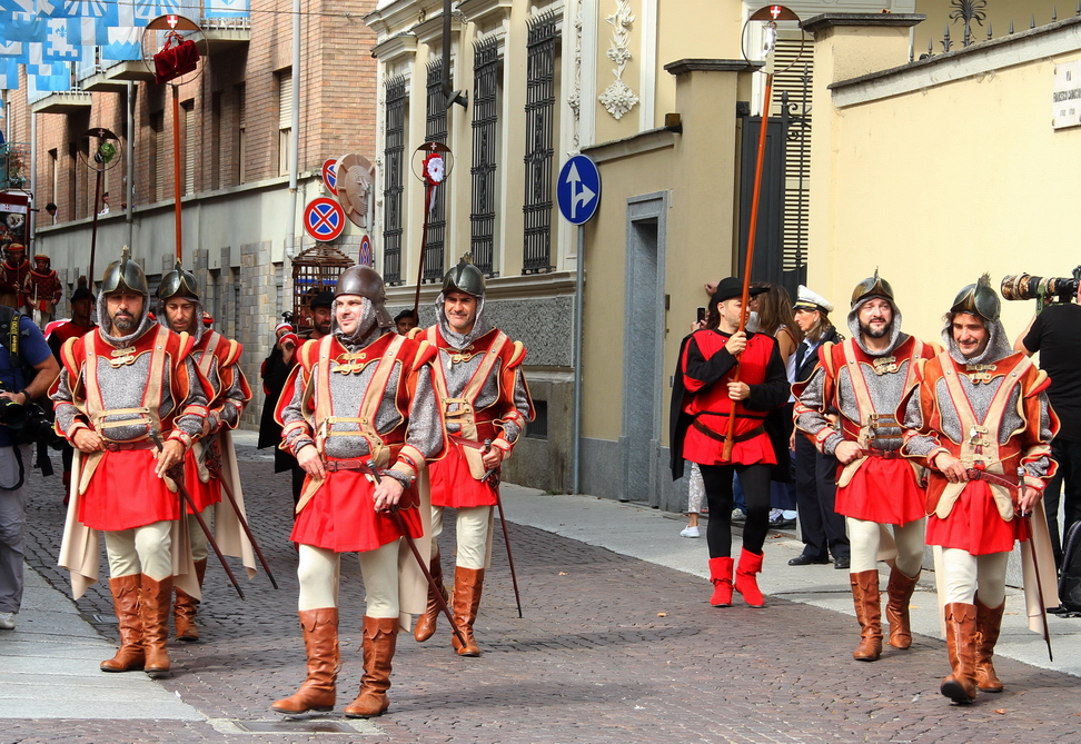 SfilataPalio_235.JPG - GRUPPO DEL COMUNE DI ASTI - Il Carroccio - Il Carroccio, elemento comunale per eccellenza, chiude il corteo ed è scortato da una schiera di armigeri in rappresentanza dei ventuno partecipanti. Il Carroccio rappresenta gli antichi carri da guerra : tuttavia la sua origine è incerta anche se alcuni storici ne fanno risalire l’utilizzo ai saraceni e ad alcune tribù germaniche. Il termine deriva dal latino medievale “Carrochium” e signiﬁca carro a funzione sia civile sia militare, utilizzato in tutta Italia all’epoca dei liberi comuni. Il Carroccio astese, trainato da tre coppie di candidi buoi, porta, come vuole la tradizione, le insegne della città - croce bianca in campo rosso - il gallo in ferro battuto, simbolo delle libertà comunali ed il Palio, ambito premio del vincitore della corsa. 