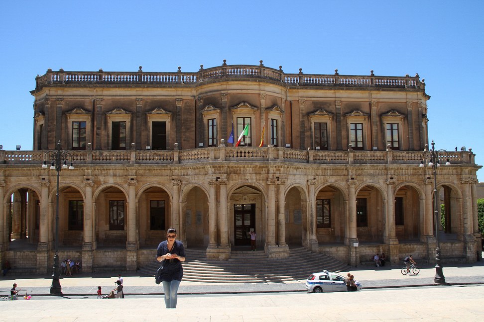 Sicilia_461.JPG - Il Municipio, centro della città, si presenta come un omogeneo quadro barocco, scandito da eleganti architetture settecentesche. Sul lato sud sorge, isolato e cinto su tre lati da un loggiato a colonne, il palazzo Ducezio, oggi sede municipale, edificio di Vincenzo Sinatra, eretto nel 1746...